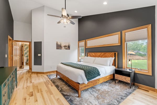 Modern bedroom featuring a wooden bed, light hardwood flooring, and large windows.