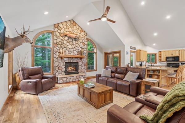Cozy living room with stone fireplace, leather sofas, and modern kitchen.