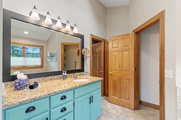 A contemporary bathroom with a turquoise vanity, granite countertop, and warm wooden accents.