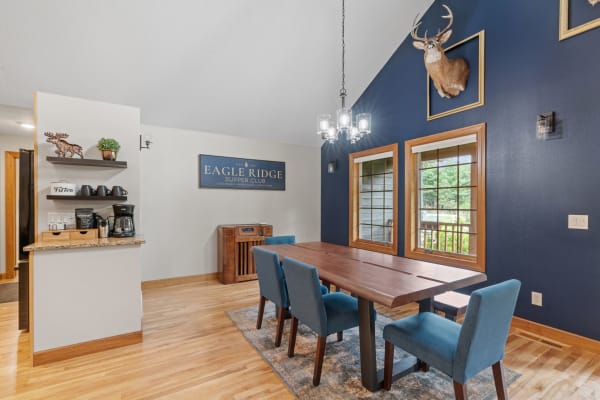 A well-decorated dining area with a wooden table, blue chairs, and rustic elements such as a deer head mount and a sign.
