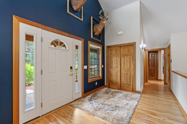 Entryway featuring a large white door, navy wall with taxidermy deer heads, wooden flooring, and a patterned rug.