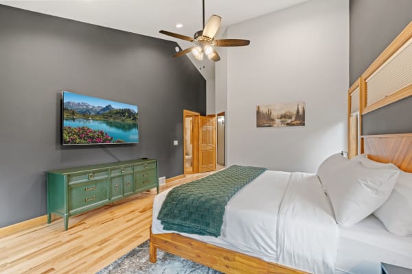 Modern bedroom with a flat-screen TV, green dresser, and cozy bedding.