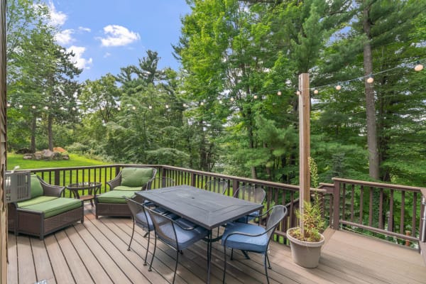 Outdoor deck with green accent chairs and a dining table surrounded by trees.