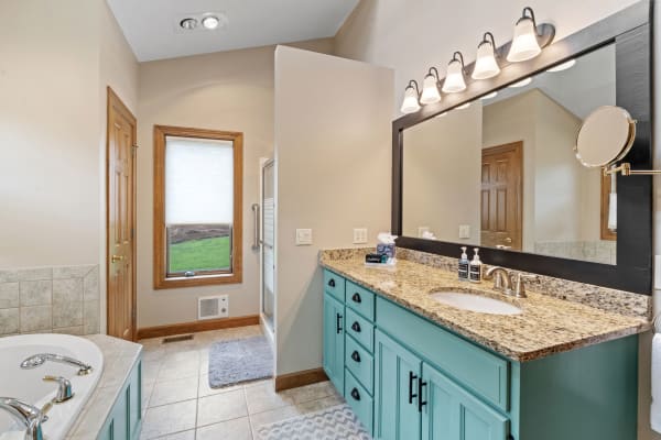 A well-designed bathroom featuring a turquoise cabinet, granite countertop, and large mirror with lighting.
