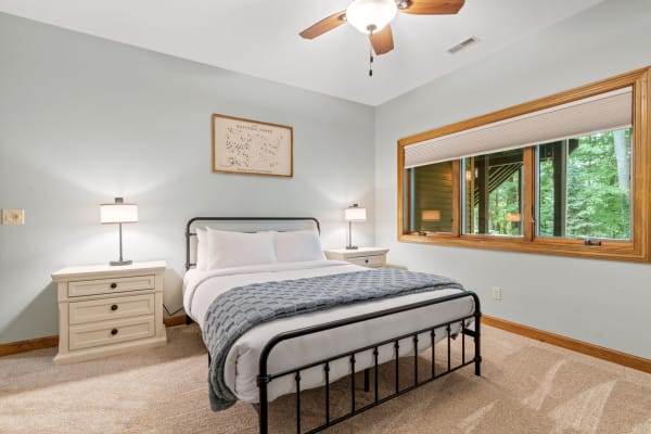 Cozy bedroom with a black metal bed, gray blanket, and a view of greenery outside.