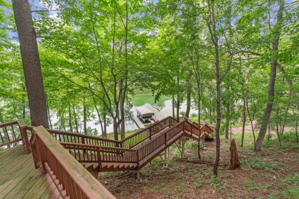 Wooden staircase in a green forest leading to a calm lake with a dock.