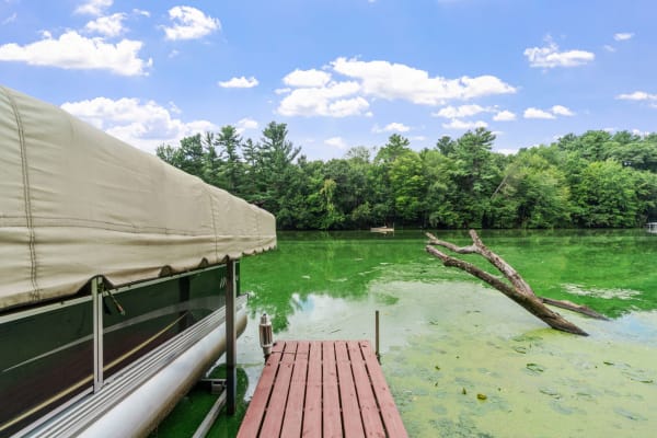 Lakeside scene featuring a dock and covered boat with green water and trees in the background.