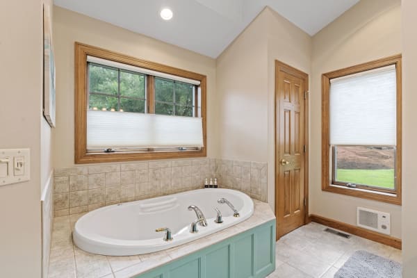 Modern bathroom with a bathtub, beige walls, and natural light from windows.