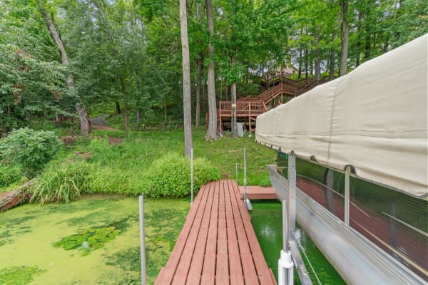 Wooden dock leading to a green, algae-covered water body with a winding path and multi-level deck in the background.