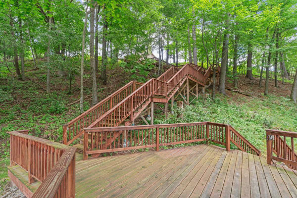 Wooden deck leading to stairs in a green forest landscape.