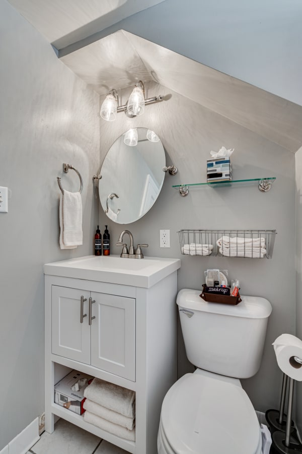 Compact bathroom with modern vanity, round mirror, and a sloped ceiling.