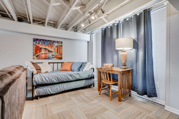 A modern basement bedroom featuring a daybed, artwork, a lamp, and wooden furniture.