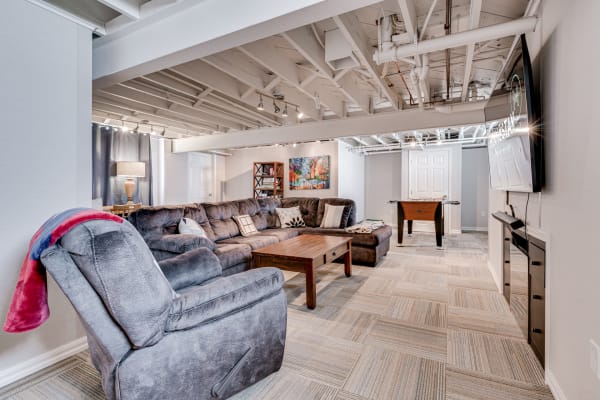 A cozy basement living room featuring a gray sectional sofa, a wooden coffee table, and a foosball table.