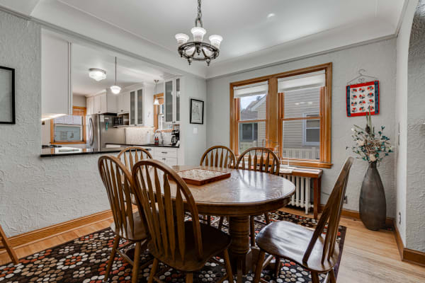 A wooden dining table surrounded by chairs, with a glimpse of a kitchen in the background.