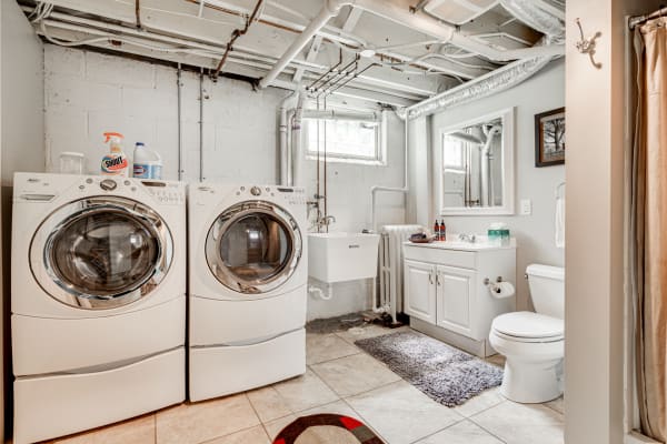Laundry and bathroom area with white washing machines, utility sink, and beige tiled floor.