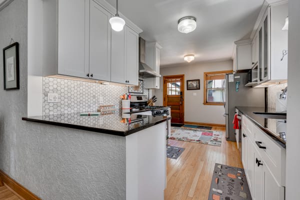 Bright kitchen with white cabinets, hexagonal backsplash, and hardwood flooring.