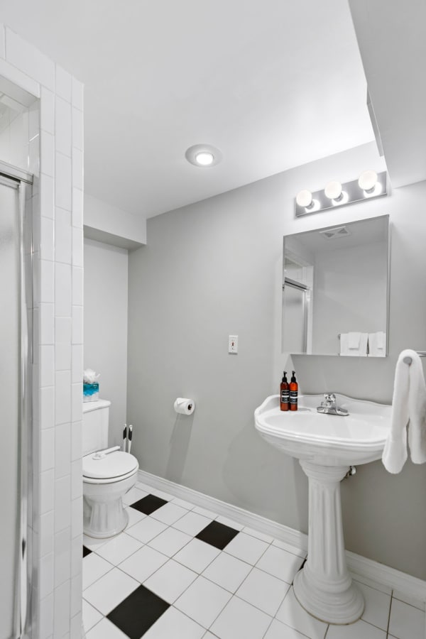 A minimalist bathroom with gray walls, black and white tiled floor, a pedestal sink, and a glass shower.