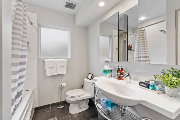 Modern bathroom with a sink, toilet, and shower area, decorated with toiletries and towels.