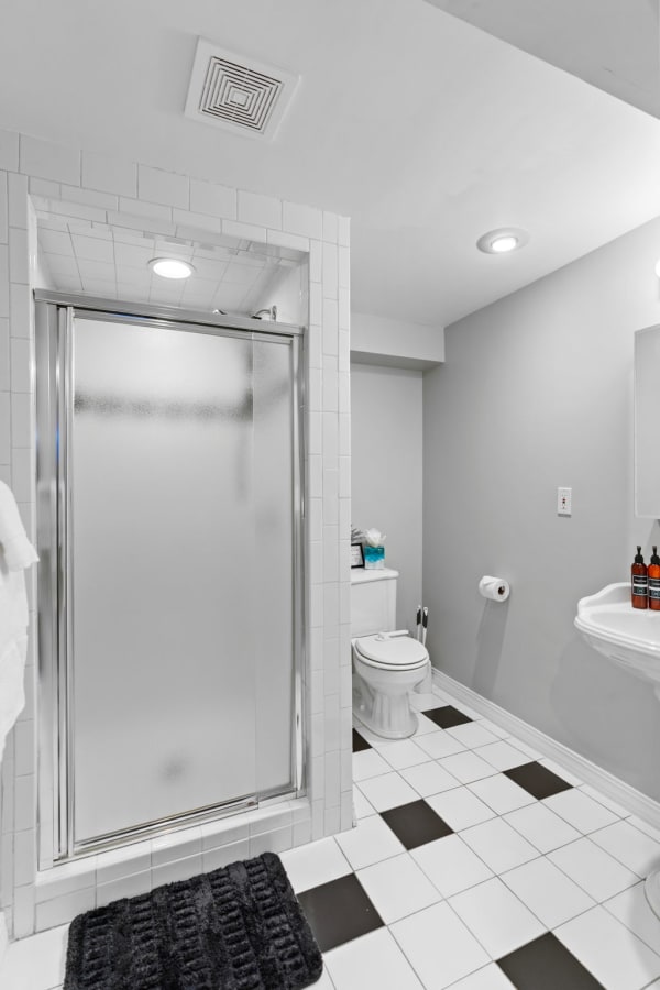 Modern bathroom with a frosted glass shower, toilet, and sink in a minimalist design.