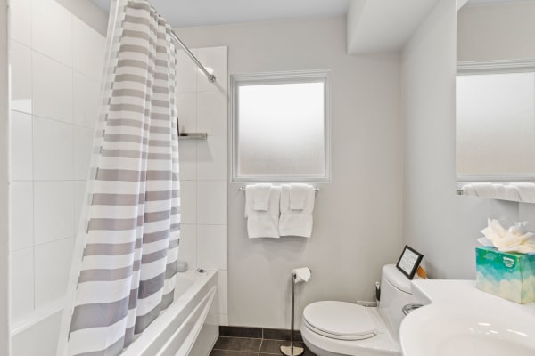 A bright bathroom featuring a bathtub with a striped shower curtain, frosted window, and white towels.