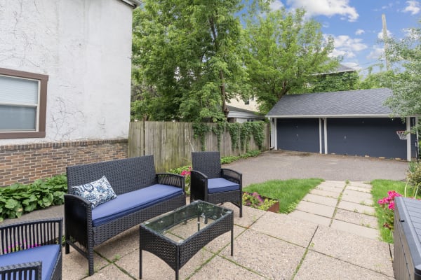 Backyard with wicker furniture, a glass table, and a garage in the background.