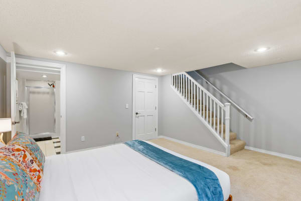 A cozy basement bedroom featuring a neatly made bed, stairs leading up, and a bathroom area.