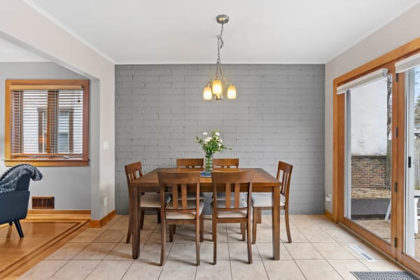 Dining area with a wooden table, chairs, and a flower vase against a gray brick wall.