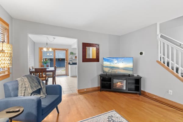 A living room with a blue armchair, TV on a black console, and a dining area with a sliding door.