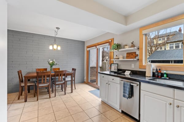A cozy kitchen with a wooden dining table, gray brick wall, and sunlight streaming through sliding doors.