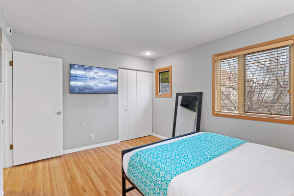 Modern bedroom featuring a bed with turquoise blanket, wooden floors, and a wall-mounted TV.