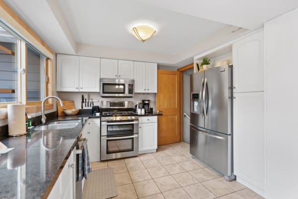 Modern kitchen with white cabinetry and stainless steel appliances, featuring a large window and a cozy arrangement.