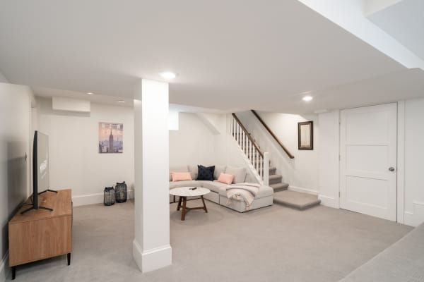 A bright and inviting basement featuring a sectional sofa, TV stand, and staircase.