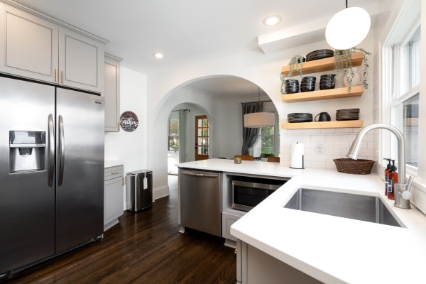 A modern kitchen with a stainless steel refrigerator, gray cabinets, white countertops, and open wooden shelves.