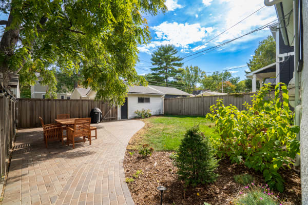 Cozy backyard featuring a brick pathway, wooden dining set, and lush plants.