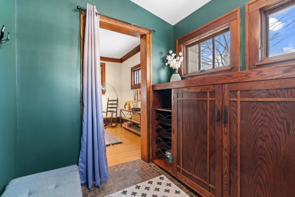 An inviting entryway featuring green walls, dark wood cabinetry, and a gray upholstered bench.