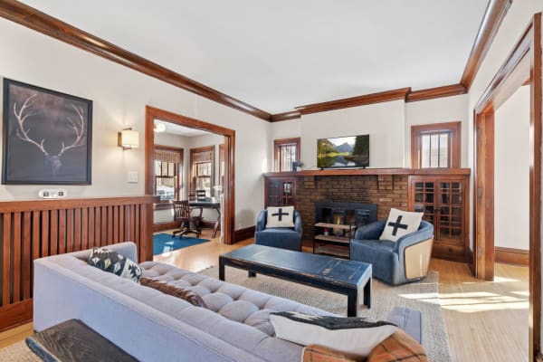 Interior view of a cozy living room featuring a gray sofa, a brick fireplace, and large windows allowing natural light.