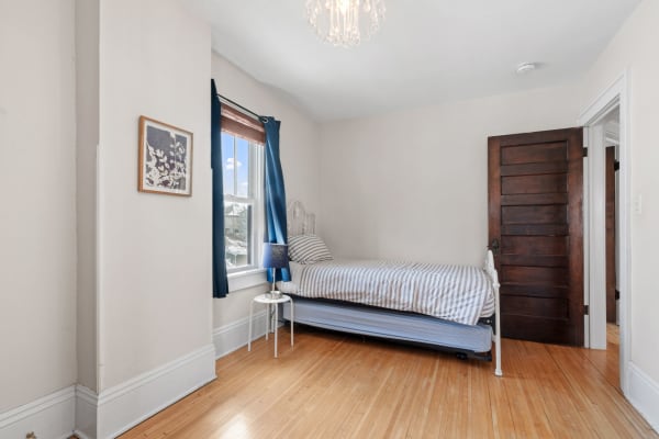 A cozy bedroom featuring a single bed, blue curtains, and wooden flooring.
