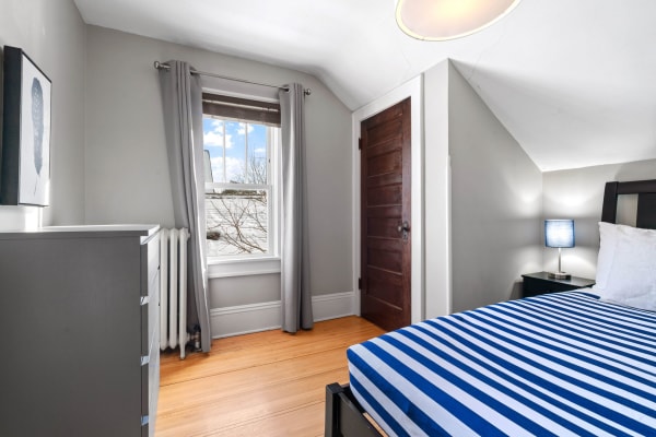 A modern bedroom with a gray color scheme, blue striped bed, and natural light streaming through the window.