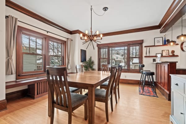 A spacious dining room featuring a large wooden table, modern chandelier, and bar area with stools.