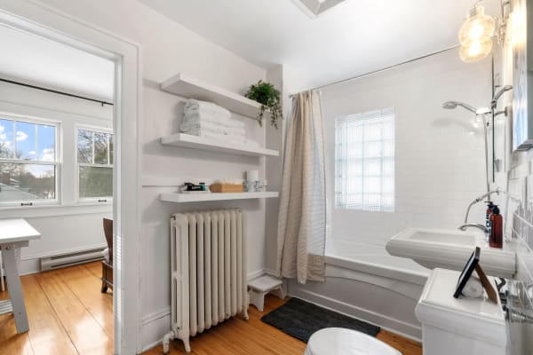 A spacious bathroom featuring white walls, a bathtub with a glass block window, and neatly arranged towels on shelves.
