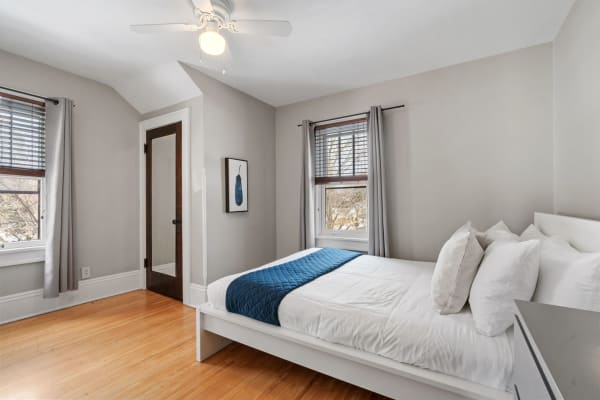 A serene bedroom with a white bed, blue quilt, and gray curtains.
