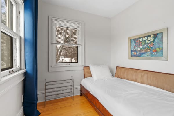 A serene bedroom with a wooden bed, white bedding, and a vibrant floral painting on the wall.