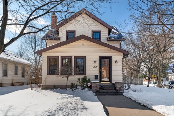 Exterior view of a two-story house with snow in front and a blue sky above.