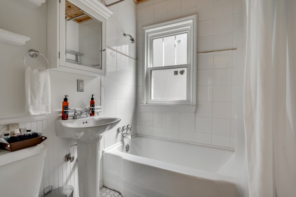 Bright and clean bathroom with white tiles, a pedestal sink, and a bathtub.