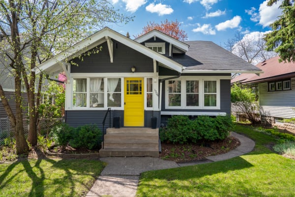 Gray house with a yellow door surrounded by greenery under a blue sky.
