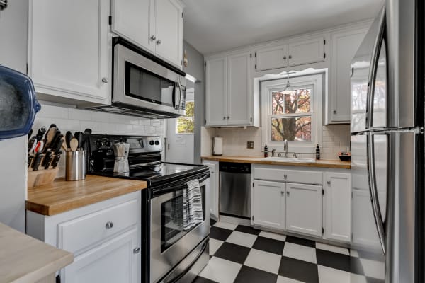 A modern kitchen with white cabinets, stainless steel appliances, and a black and white checkered floor.