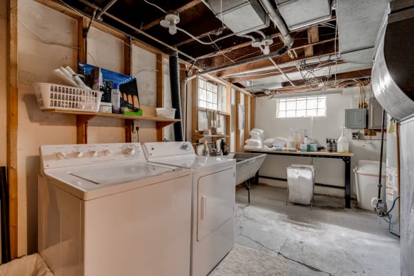 Interior view of a basement laundry room featuring a washing machine and dryer, storage shelves, and cleaning supplies.