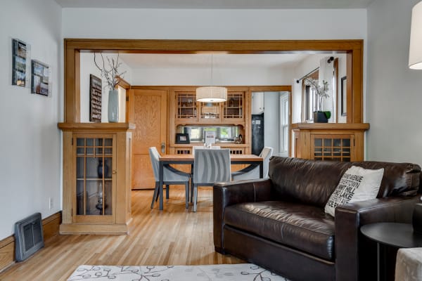 Cozy living room with a dark leather couch and an archway leading to a dining area with a wooden table and gray chairs.