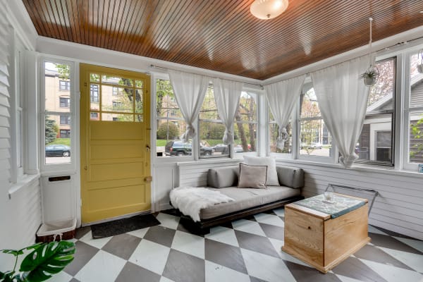 A sunroom featuring a yellow door, gray couch, and wooden accents.