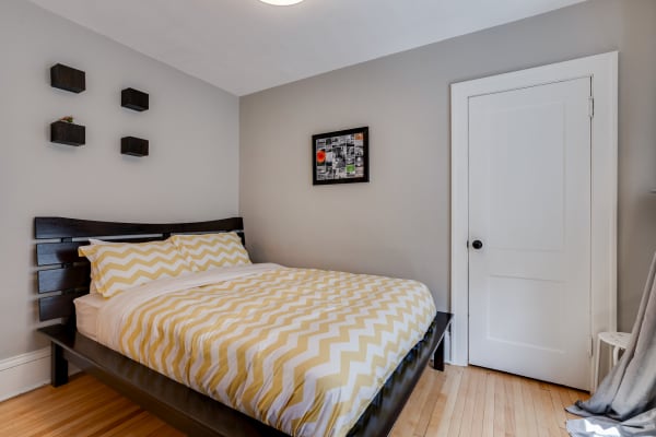 A well-decorated bedroom featuring a black bed with chevron bedding, light gray walls, and wooden shelves.